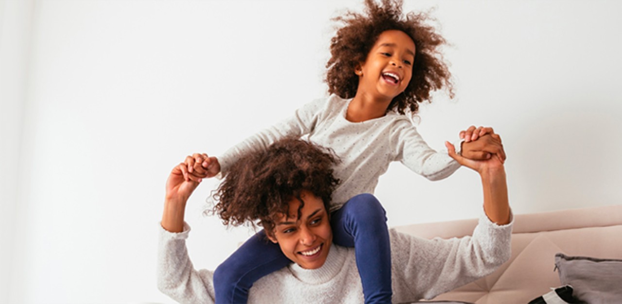 Photo d’une femme souriante avec son enfant sur ses épaules 