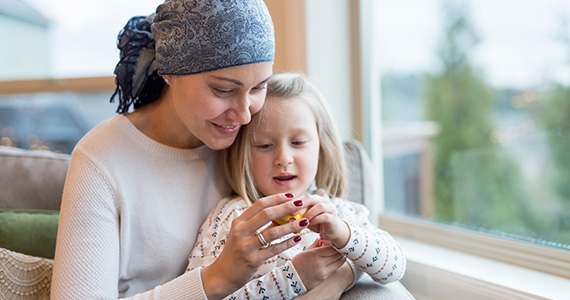 Femme atteinte du cancer du sein qui joue avec sa fille assise sur ses genoux.