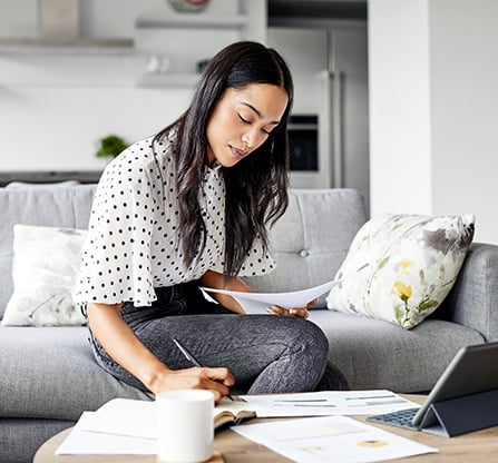 Photo d’une femme dans son salon qui travaille sur des documents devant son ordinateur portable