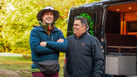 Photo d’un expert et de son client souriant à côté d’une minifourgonnette de camping 