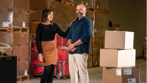 Photo d’une experte et de son client souriant dans un entrepôt rempli de boîtes 