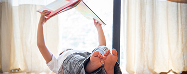 Enfant allongé sur le dos tient un livre à bout de bras