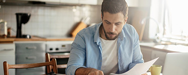 Homme regarde des papiers dans sa cuisine