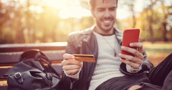 Jeune homme assis sur un banc tient une carte de crédit et un téléphone