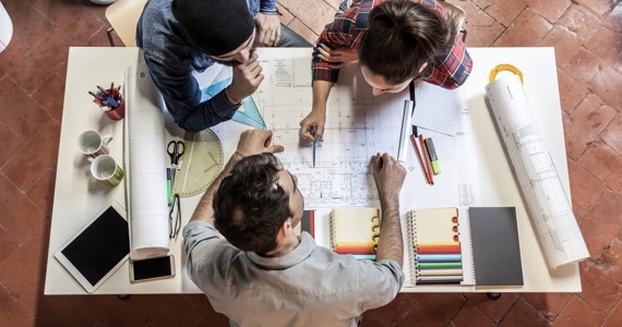 Jeune couple regarde le plan d’une maison avec un architecte