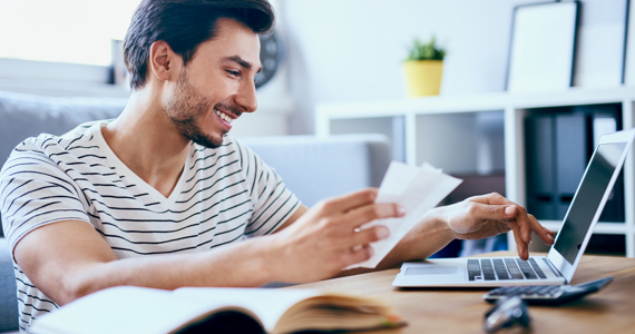 Jeune homme tient des notes et utilise son ordinateur portable