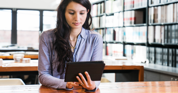 Jeune femme à la bibliothèque regarde sa tablette