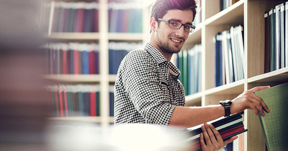 Jeune homme debout devant une bibliothèque sourit