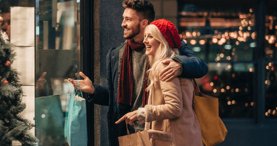 Photo d'un couple souriant avec des sacs qui regarde une vitrine de magasin 