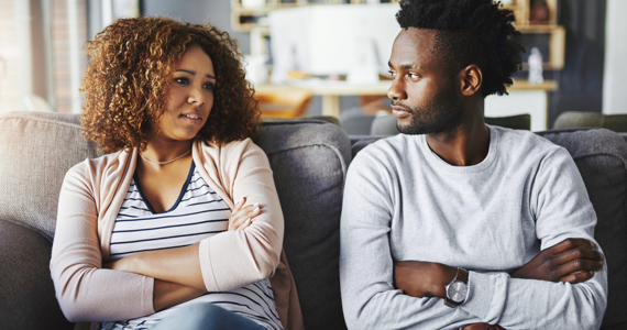 Jeune femme et jeune homme qui ont les bras croisés discutent sur un divan