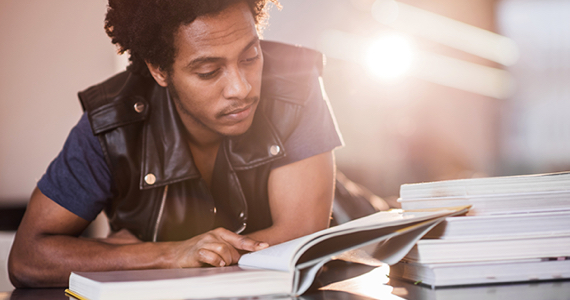 Jeune étudiant avec blouson de cuir lit dans une bibliothèque