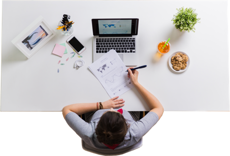 Photo d'une personne assise à un bureau devant un ordinateur portable qui écrit sur une feuille de papier