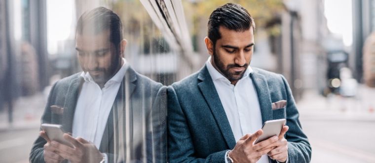 Photo d’un homme qui consulte son cellulaire devant un immeuble à bureaux