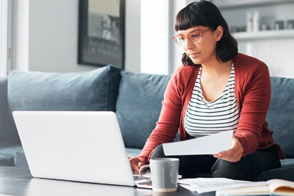 Jeune femme assise sur son canapé et qui regarde son ordinateur
