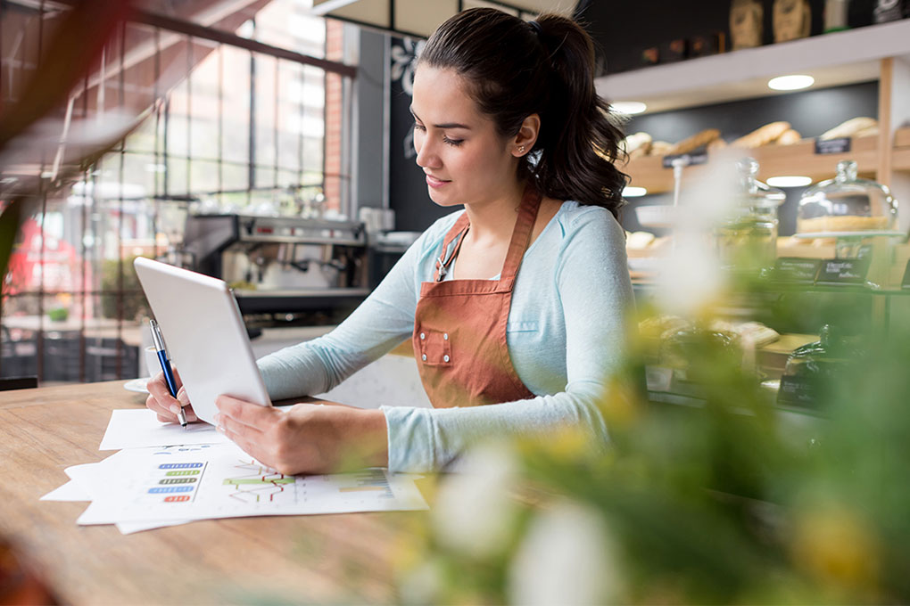 Une femme se tient devant un ordinateur portable. Elle prend des notes avec un crayon.