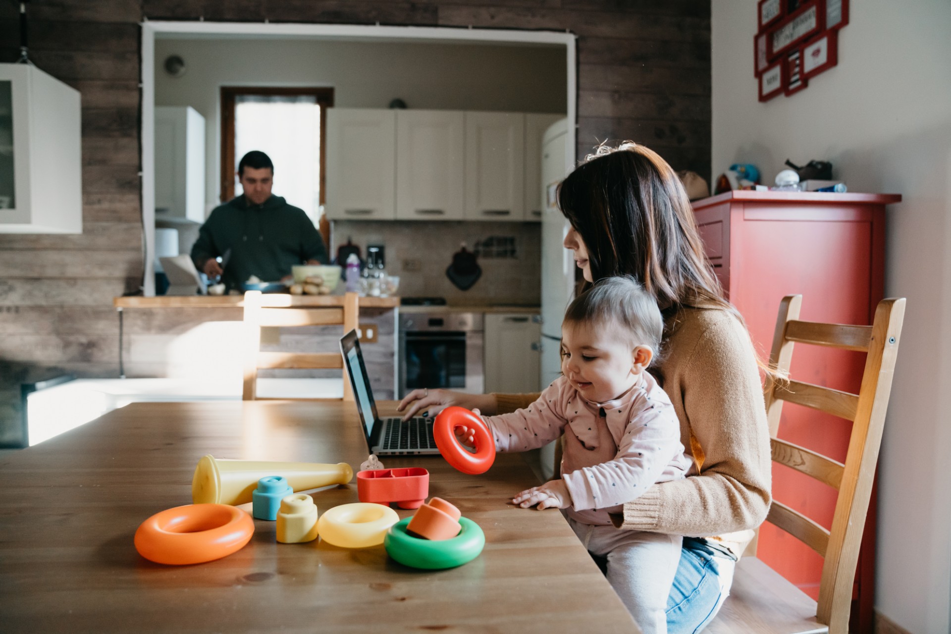 Maman assise à table devant son ordinateur et qui tient son bébé sur ses genoux