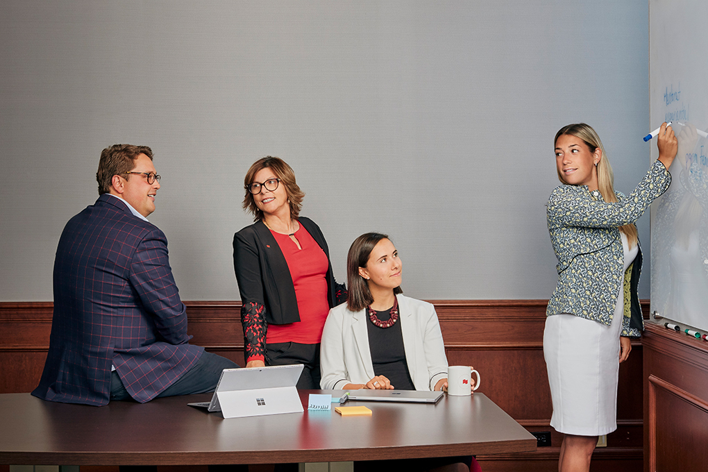 Photo d’une femme écrivant au tableau dans un bureau devant un homme et deux femmes en tenue professionnelle 