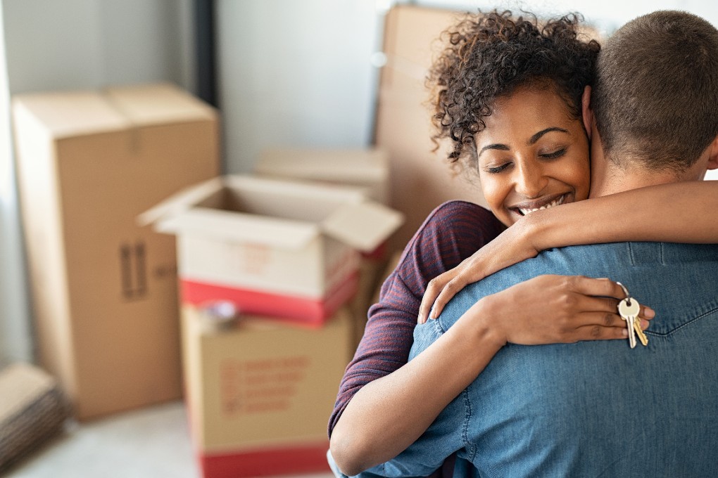 Un couple de nouveaux propriétaires se serre dans les bras après avoir pris possession de leur maison.