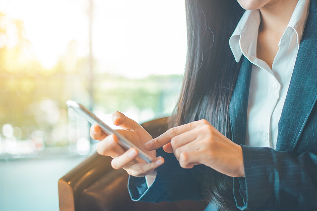 Image d’une main de femme qui tient son téléphone cellulaire et une tasse de café sur la table.