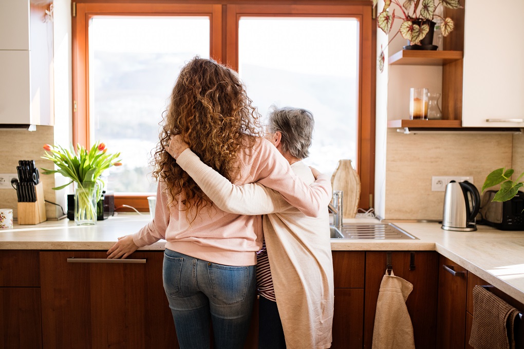 Mère et fille se serrant l'une contre l'autre, regardant par la fenêtre de la cuisine