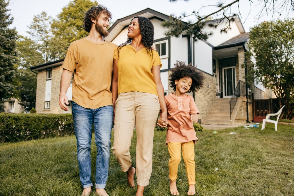 Photo d’un couple avec leur fillette se tenant par la main devant leur maison