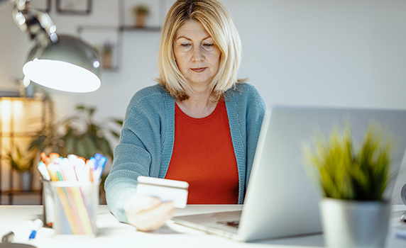 Photo d’une femme consultant sa carte de crédit devant son ordinateur portable
