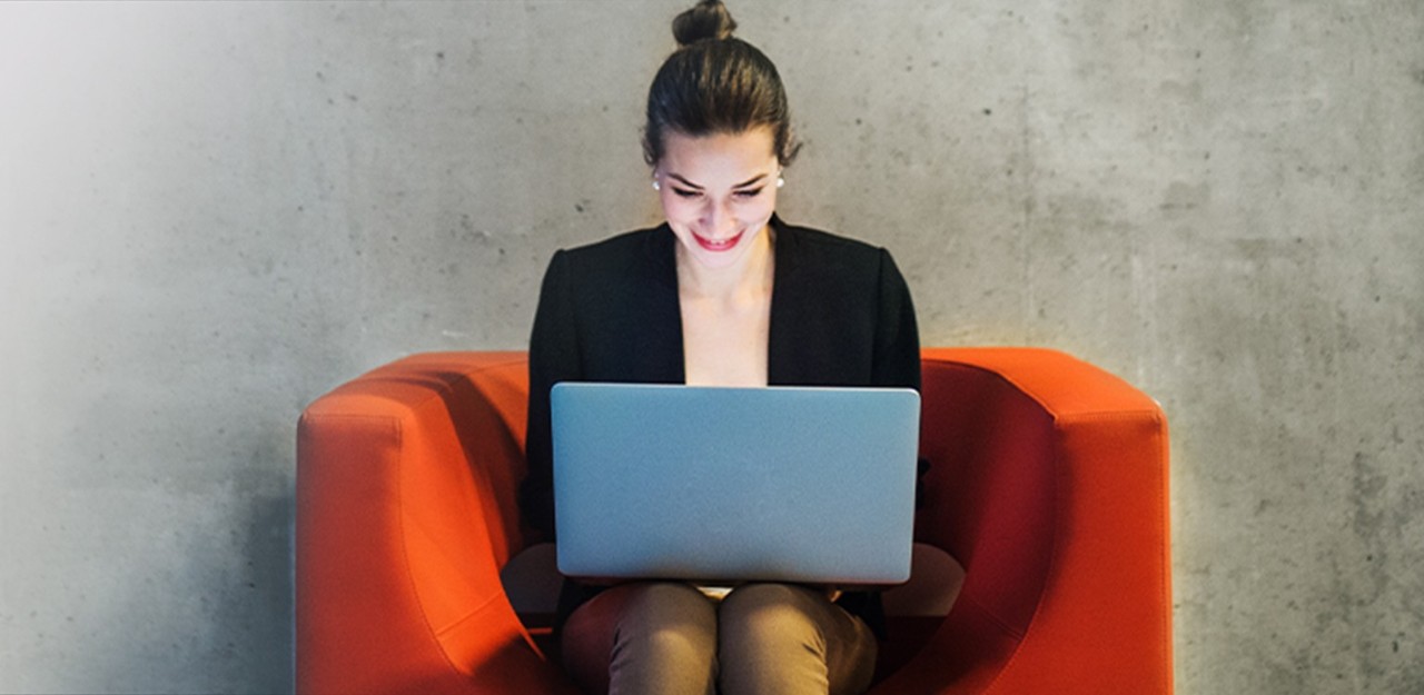 Photo d’une femme assise sur un fauteuil qui consulte son ordinateur portable en souriant