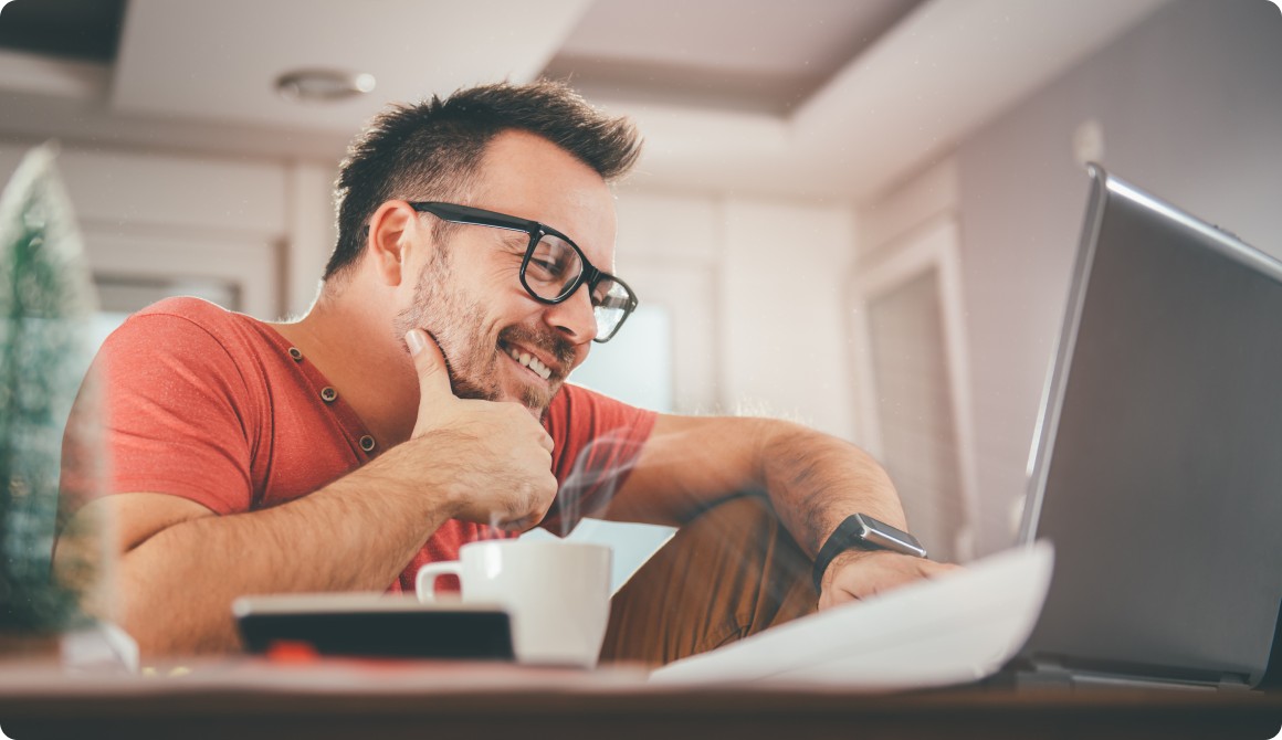 Photo d’une personne souriante devant son ordinateur avec un café