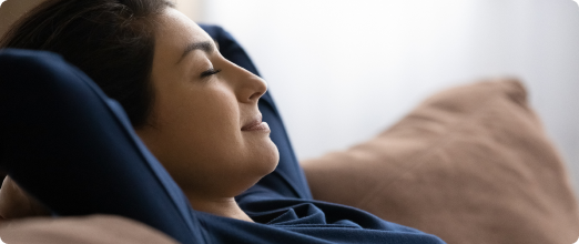 Photo d’une femme les yeux fermés avec les bras derrière la tête sur un sofa