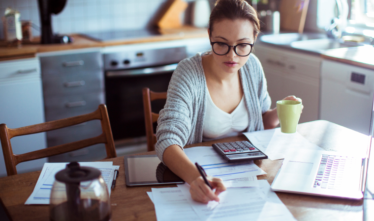 Photo d’une femme qui consulte des documents en buvant du café dans sa cuisine