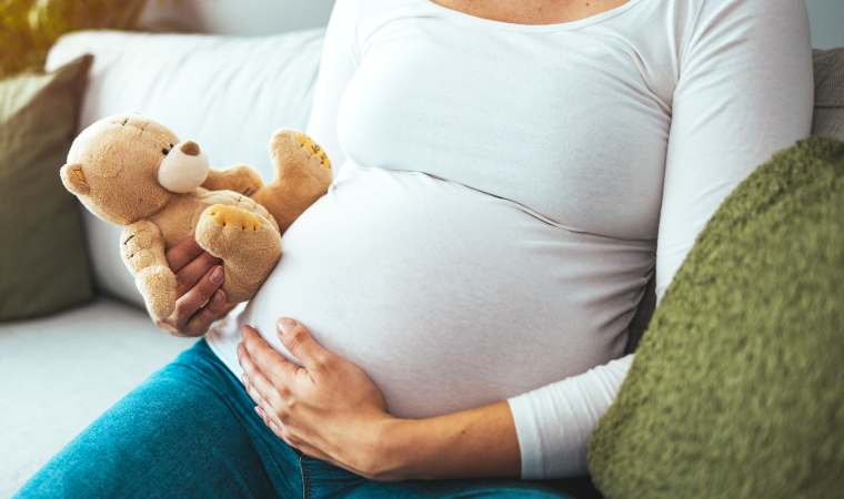 Photo en gros plan du ventre d’une femme enceinte assise tenant un ourson de peluche
