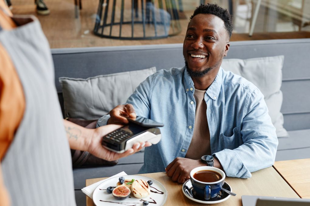 Photo d’une personne souriante qui paie avec sa carte de crédit dans un café 