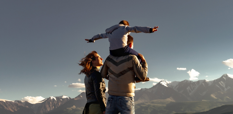 Photo de deux adultes faisant face à la montagne avec un enfant sur les épaules