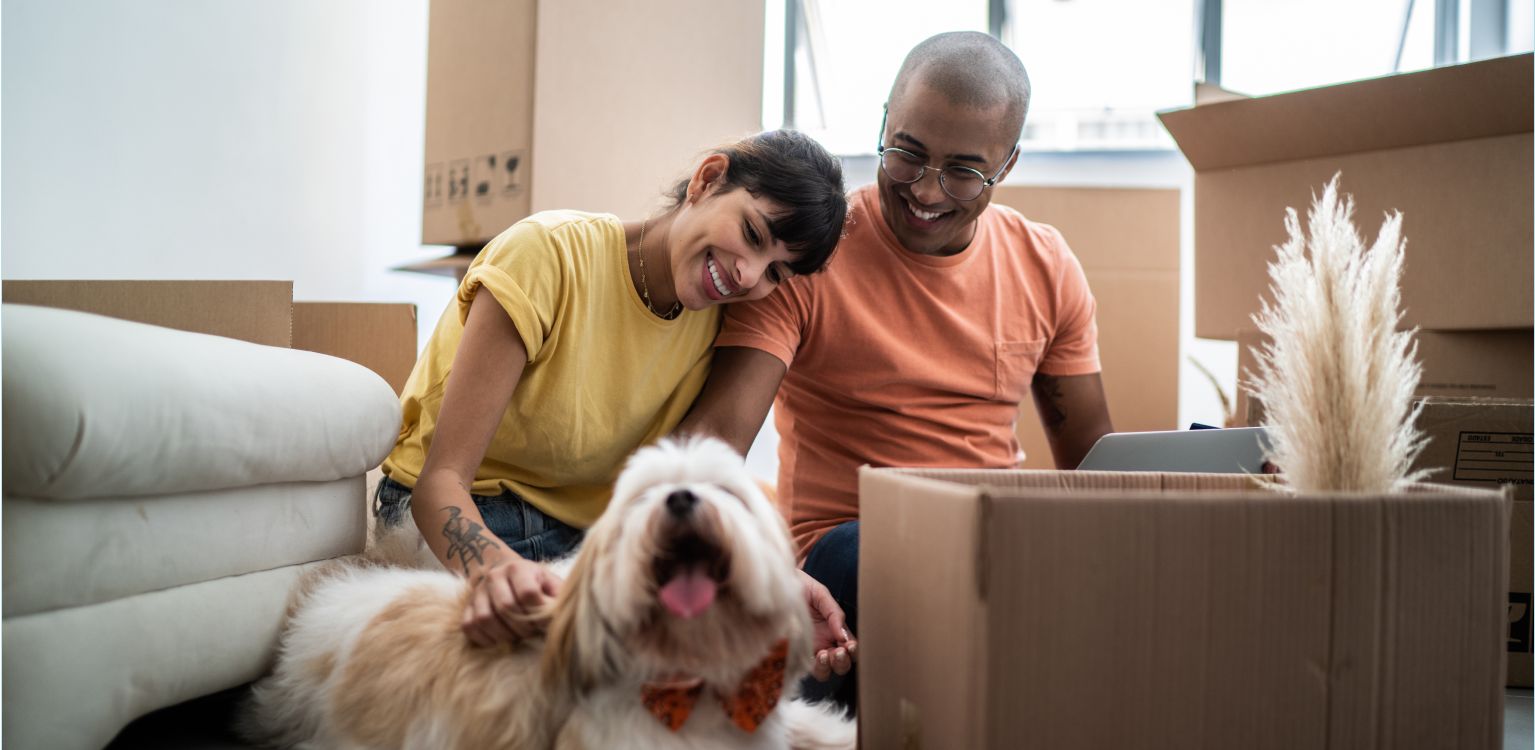 Jeune couple assis avec un chien qui est entouré de boîtes de déménagement en carton 